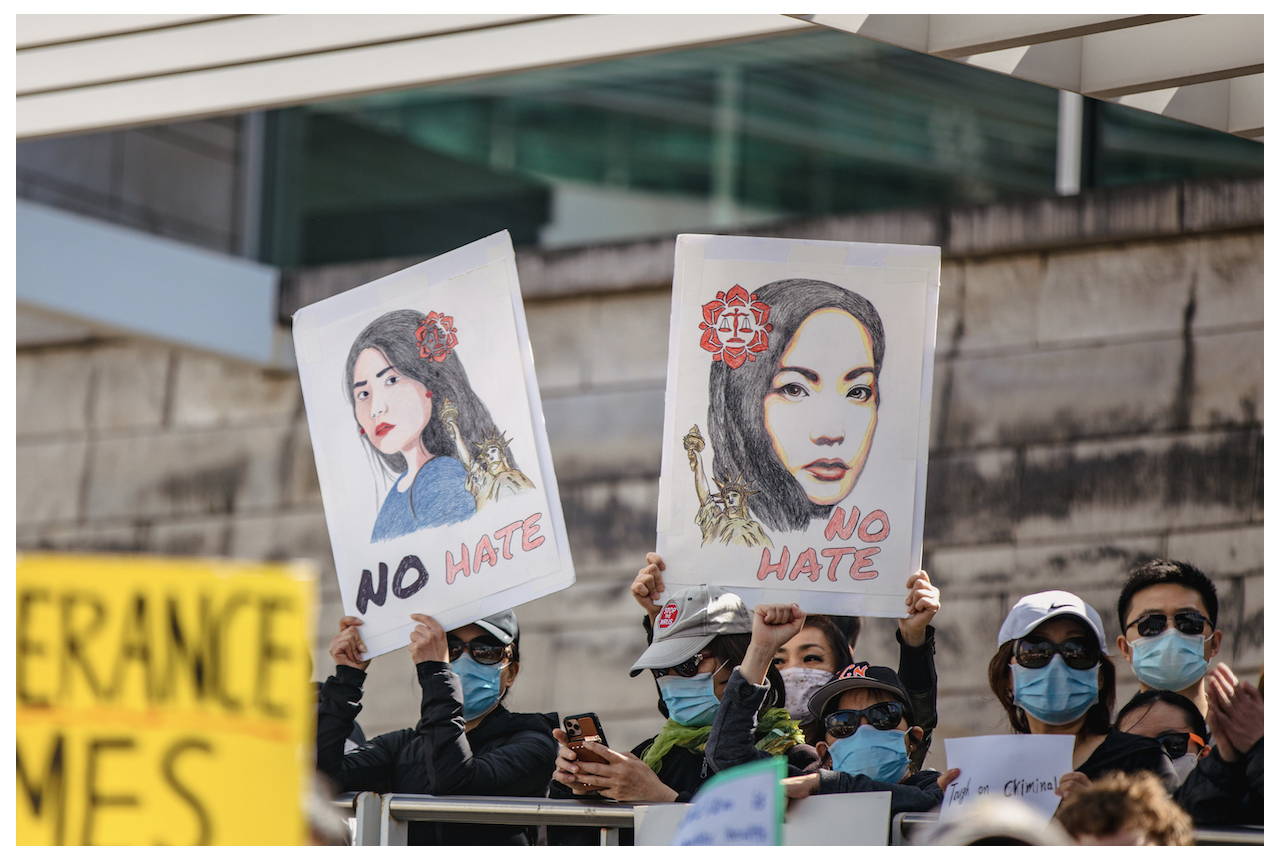 In center photo, two drawings of women of Asian descent with the words "NO HATE" written below them. These drawings are being held up by people in a rally outdoors.