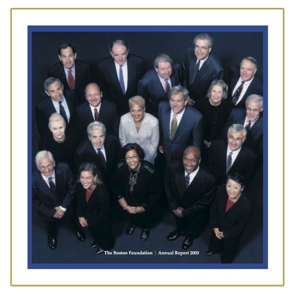 TBF leadership all wearing dark colored clothing, standing on a dark blue floor, looking up at the camera, smiling